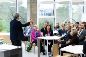 A man delivers a presentation to an audience, gesturing.