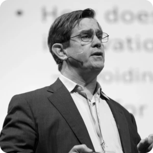 Prof. Henry Chesbrough, Faculty Co-director at the Garwood Center for Corporate Innovation, UC Berkeley. Portrait photograph of a man wearing glasses, a suit jacket, and a light-colored shirt while speaking at an event. He is shown in profile against a blurred presentation background.