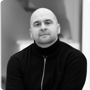 Prof. &Scaron;arūnas Grigaliūnas, Head of the National Cyber Security Centre of Excellence at KTU. Portrait photograph of a man with closely cropped hair wearing a dark high-neck sweater. He is seated facing the camera with a softly blurred indoor background.