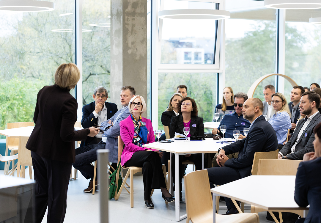 Speaker addressing a seated audience of business and academic professionals during a discussion at the Open Innovation Centre forum.