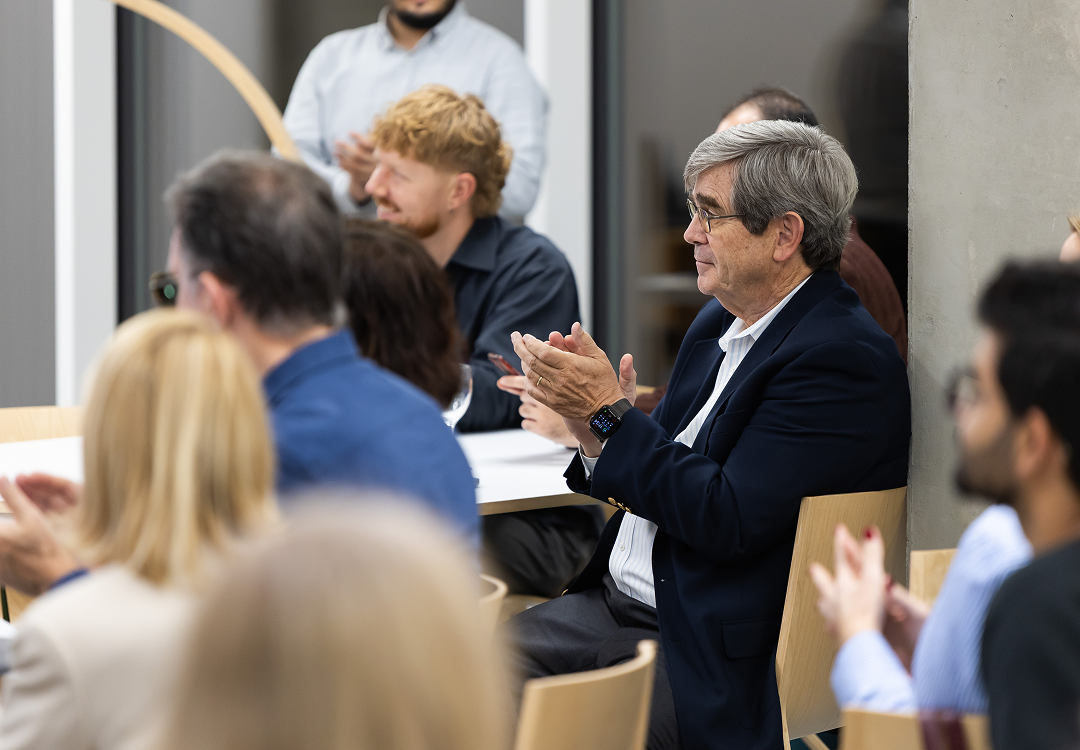 Seated forum participant applauding during an Open Innovation Centre session as other attendees around him join in.