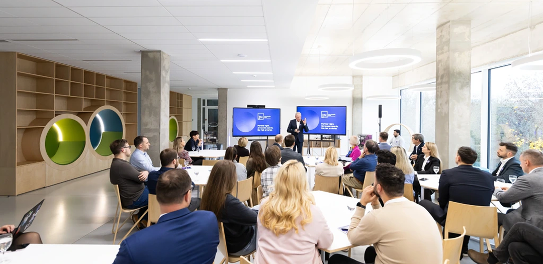 Innovation now requires coordination across partners A speaker addresses an audience seated at tables in a bright, modern conference room, with KTU Open Innovation Centre branding displayed on screens.