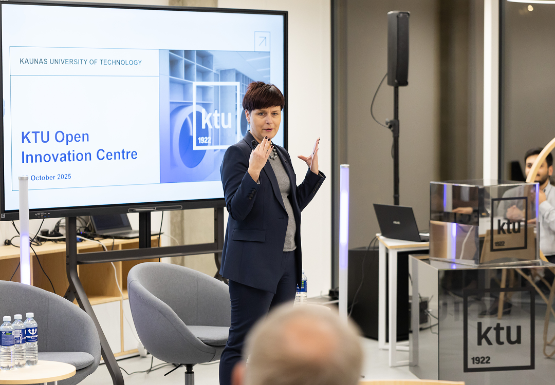 OIC for Technology & ecosystem connection Woman in a dark suit speaking and gesturing during a presentation, with the KTU logo displayed on a screen behind her.