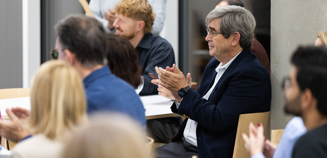 Wrong innovation decisions are expensive Group of people seated in a modern conference setting, applauding during a presentation or discussion.