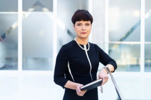 dark-haired woman dressed in black standing against grey background